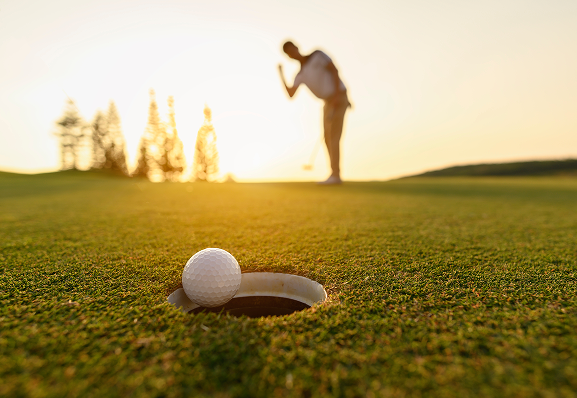 golf ball falling into hole with man in background
